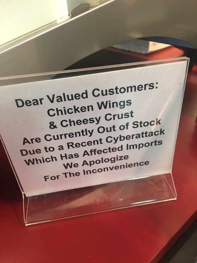 A sign on the counter of a fast-food restaurant reading “Dear Valued Customers: Chicken Wings & Cheesy Crust Are Currently Out of Stock Due to a Recent Cyberattack Which Has Affected Imports We Apologise For The Inconvenience”