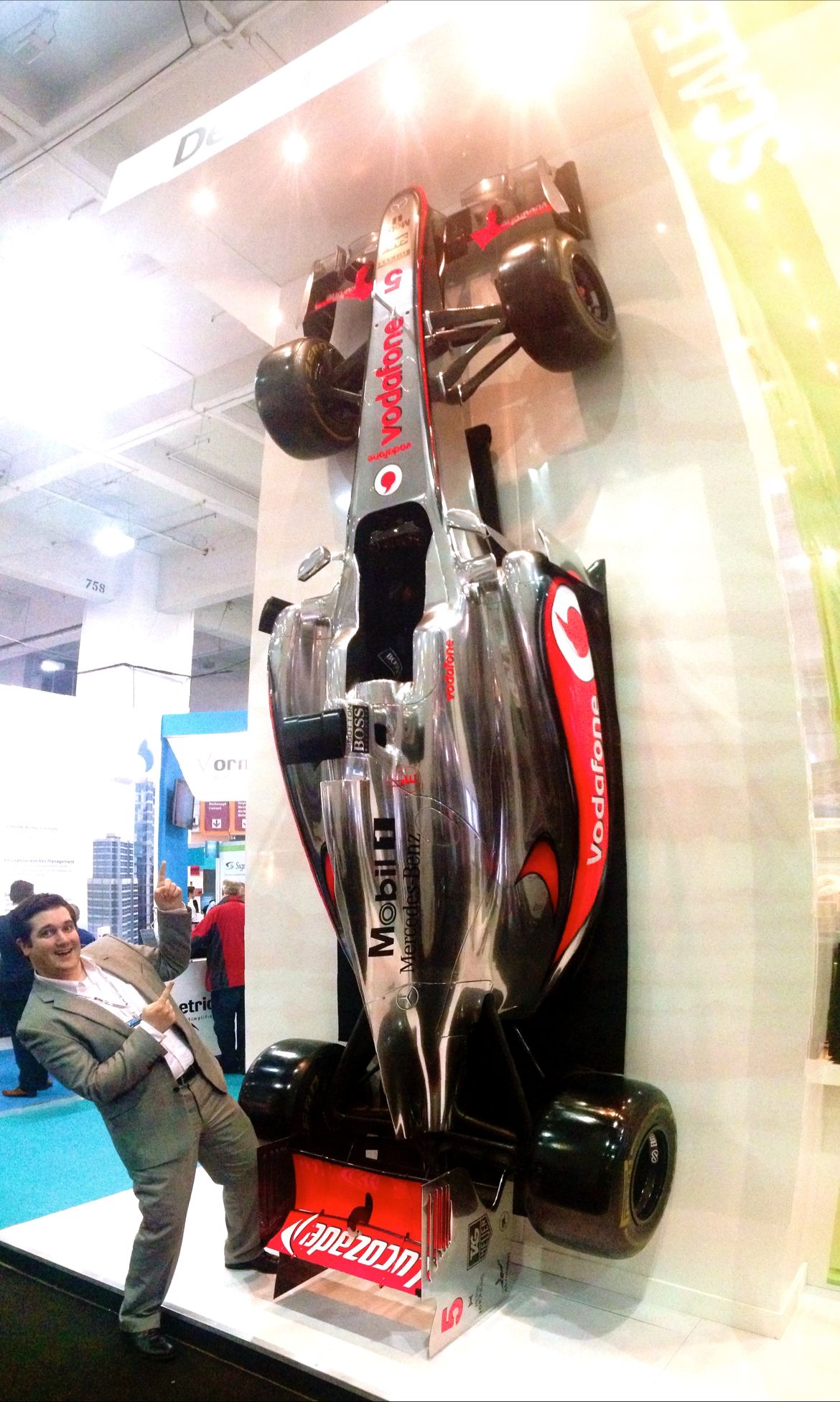 A McLaren Mercedes formula 1 car is mounted vertically to Detica’s 2013 stand at Infosec dwarfing Robin in the foreground pointing at it